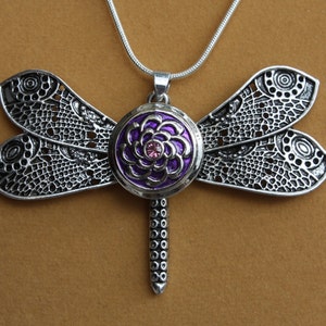 May include: A silver-toned dragonfly pendant necklace. The dragonfly features intricate openwork wings and a central purple and pink floral design. The pendant hangs from a delicate silver chain.