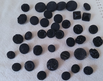 Può includere: Una collezione di 30 bottoni in vetro nero con vari disegni intricati. I bottoni sono rotondi e hanno una finitura liscia e lucida.
