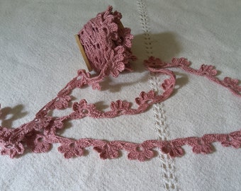 May include: A spool of dusty rose crochet trim with a delicate floral design. The trim is made of a soft, lightweight material and is perfect for adding a touch of elegance to any project.