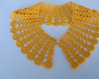 Puede incluir: Un collar de ganchillo amarillo con un borde festoneado y un pequeño botón de perla en el centro.