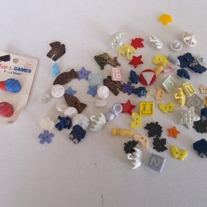 May include: A collection of assorted buttons in various shapes and colors, including stars, flowers, and geometric designs. Some buttons are on a card labeled "Fun & Games" with boxing glove designs.