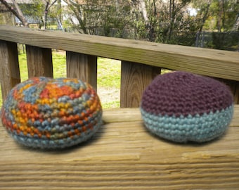 Könnte beinhalten: Zwei gehäkelte Kugeln, eine mit einem blauen, orangefarbenen und braunen Muster und die andere mit einem violetten und blauen Muster.
