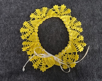 Puede incluir: Un collar de ganchillo amarillo con una cinta blanca atada en un lazo en el centro.