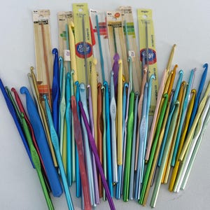May include: A collection of crochet hooks in various colors, including blue, green, yellow, and purple. Some hooks are still in their original packaging. The hooks are made of metal and plastic, and are of different sizes.
