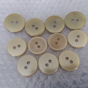 May include: Ten beige plastic buttons with two holes each. The buttons are round and have a smooth, glossy finish.