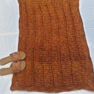 May include: A crocheted throw blanket in shades of orange and brown. The blanket has a textured, ribbed pattern.