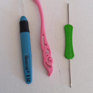 May include: Three crochet hooks in different colors. A blue hook with a black grip and the text "The Crochet Lite" and "5.5 mm". A pink hook with a decorative handle. A green hook with the text "0/8".