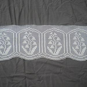 May include: White crocheted window valance with a floral design. The valance has four sections with a repeating pattern of flowers.