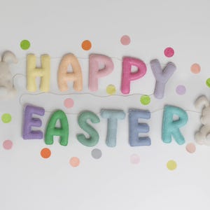May include: A pastel-colored felt banner with the words "Happy Easter" and two white felt bunny rabbits on either end. The banner is decorated with colorful confetti dots.