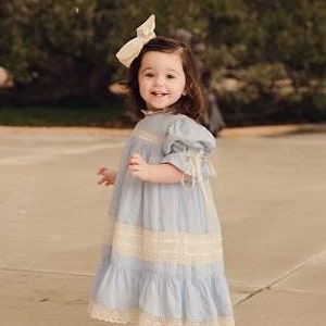 Puede incluir: Una ni&ntilde;a peque&ntilde;a con un vestido azul claro con ribete de encaje blanco y un lazo blanco en el pelo.