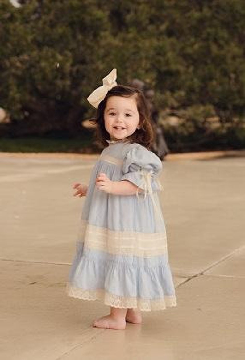 Puede incluir: Una ni&ntilde;a peque&ntilde;a con un vestido azul claro con ribete de encaje blanco y un lazo blanco en el pelo.
