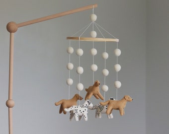 May include: A wooden baby mobile featuring tan and white felt dog figures and cream-colored felt balls. The mobile hangs above a white crib, creating a soft, neutral nursery decor.