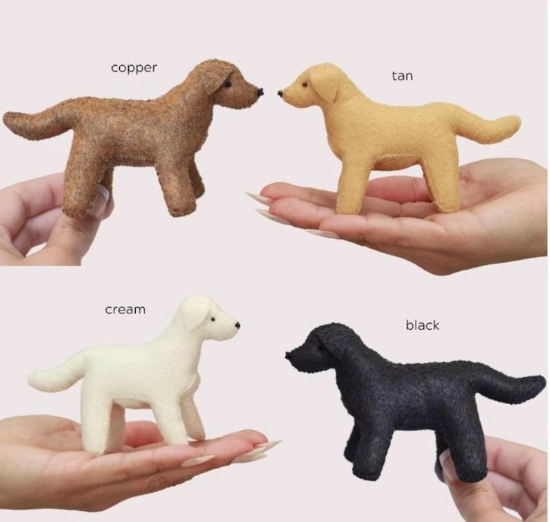 Op de afbeelding: Vier vilten hondenbeeldjes in koper, bruin, cr&egrave;me en zwart. Elke hond staat, met de kleurnaam erboven. De honden zijn klein en lijken handgemaakt.
