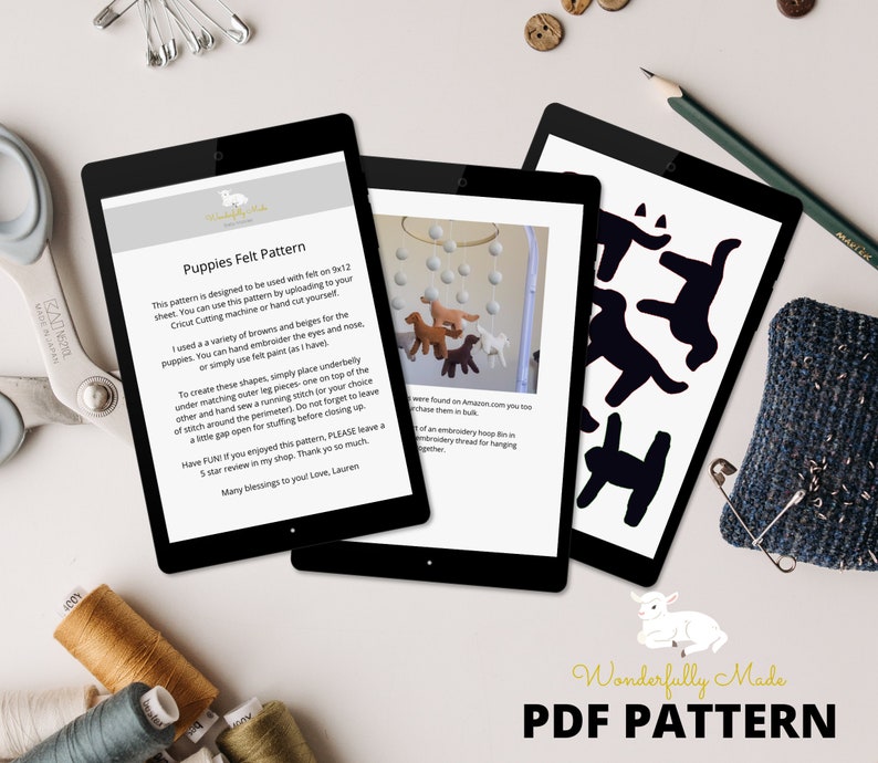 Op de afbeelding: Drie tablets tonen een digitaal PDF-patroon voor vilten puppy's. Het patroon bevat instructies voor handborduurwerk of viltverfdetails. De afbeelding toont ook knutselgereedschap zoals schaar, draad en een speldenkussen.