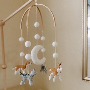 May include: A wooden baby mobile with a crescent moon, white pom poms, and felt animal figures. The animals include a grey and white cat, a brown and white dog, and a brown and white dog with a black nose.