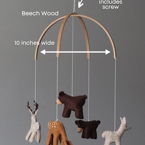 May include: A wooden mobile with a 10-inch wide beech wood frame. The mobile features five felt animal figures: two deer, two bears, and one fawn. The mobile includes a screw for hanging.