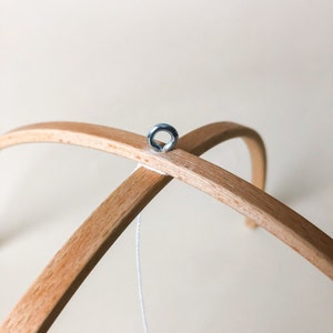 May include: A wooden mobile frame with a metal ring attached to the top. A white string hangs from the ring.