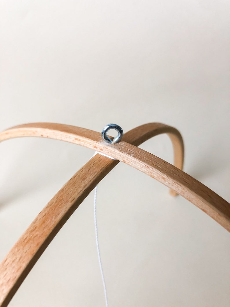 May include: A wooden mobile frame with a metal ring attached to the top. A white string hangs from the ring.