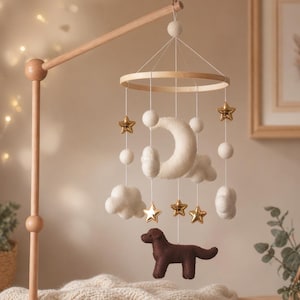 Op de afbeelding: Een houten baby mobile met een halve maan, wolken, sterren en een bruine hond. De mobiel heeft een houten frame en is opgehangen aan een houten arm. De sterren zijn goudkleurig en de wolken en maan zijn wit.