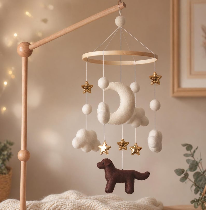 Op de afbeelding: Een houten baby mobile met een halve maan, wolken, sterren en een bruine hond. De mobiel heeft een houten frame en is opgehangen aan een houten arm. De sterren zijn goudkleurig en de wolken en maan zijn wit.