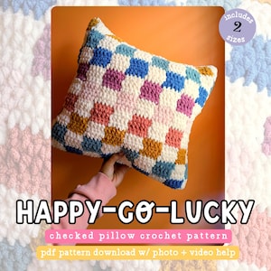 May include: A crochet pillow pattern featuring a checkered design in shades of blue, pink, white, and orange. The pattern includes two sizes and comes with a PDF download, photo, and video instructions. "HAPPY-GO-LUCKY" is written in bold letters below the pillow.