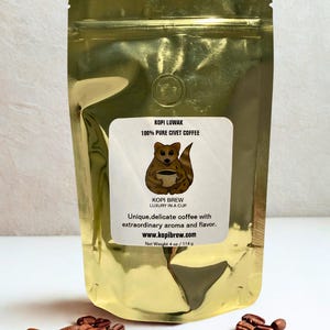 May include: A gold foil coffee bag with the text "KOPI LUWAK 100% PURE CIVET COFFEE" and a cartoon civet cat holding a cup of coffee. The bag also includes the text "KOPI BREW LUXURY IN A CUP" and "Unique, delicate coffee with extraordinary aroma and flavor." The net weight is 4 oz.