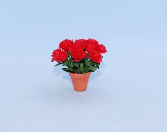 May include: A miniature potted plant featuring a cluster of vibrant red rose blossoms with small green leaves, housed in a simple, unglazed terracotta-coloured clay pot. The arrangement is compact and displays multiple detailed flower heads.