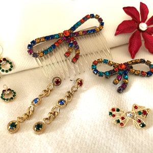 May include: A set of colorful jeweled hair clips and earrings. The hair clips are in the shape of bows and the earrings are in the shape of circles and chains.
