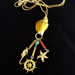 May include: Gold necklace with a seashell pendant and charms, including a starfish, a seahorse, and a ship's wheel.