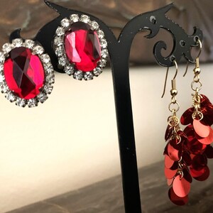 May include: A pair of red rhinestone earrings and a pair of dangle earrings with red sequins.