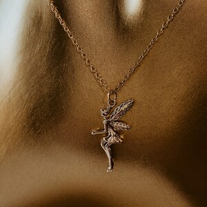 May include: A gold chain necklace with a fairy pendant. The fairy is depicted with wings and a flowing dress.