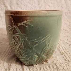 May include: A green ceramic planter with a brown glaze and a raised design of pine branches and cones.