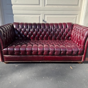May include: A burgundy leather Chesterfield sofa with a button-tufted design. The sofa has rolled arms and a low profile. The sofa is approximately 84 inches long.