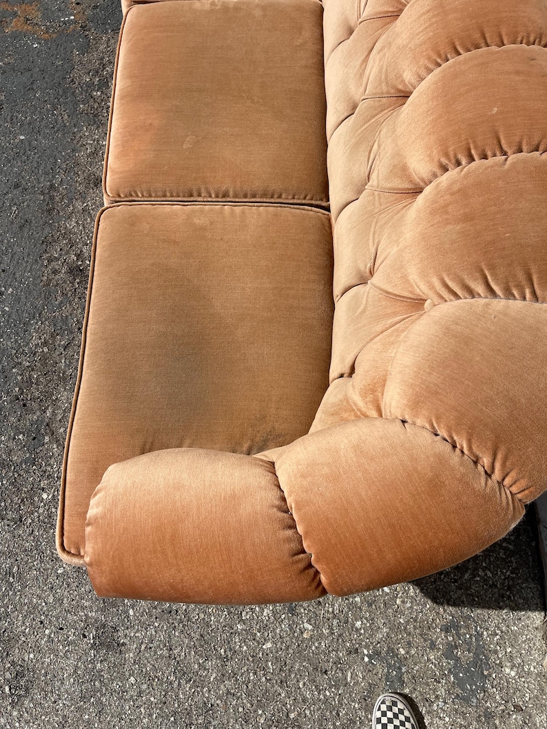 May include: A brown tufted velvet sofa with a curved armrest. The sofa has a classic design and is upholstered in a soft, plush fabric.