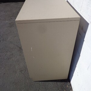 May include: Two beige file cabinets stacked on top of each other. The cabinets have a simple design and are made of a smooth material.