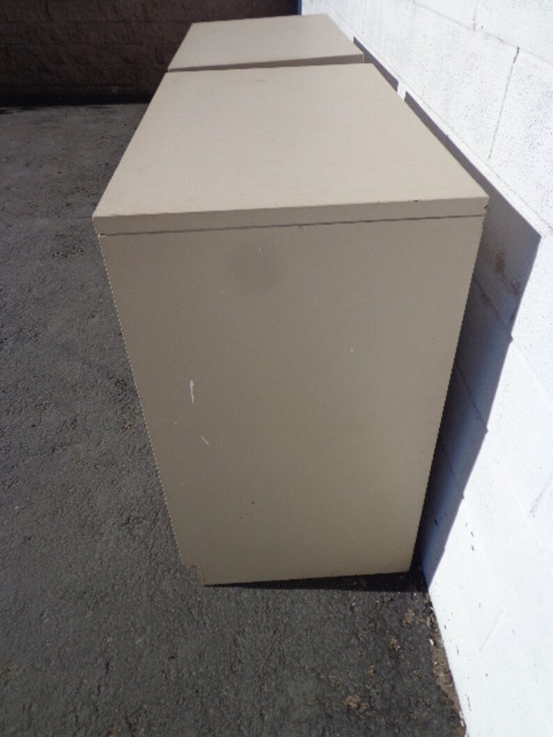 May include: Two beige file cabinets stacked on top of each other. The cabinets have a simple design and are made of a smooth material.