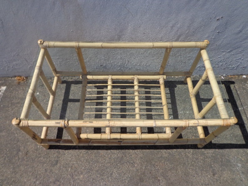 May include: A rectangular bamboo coffee table with a glass top. The table has a simple design with a woven bamboo base and a clear glass top.