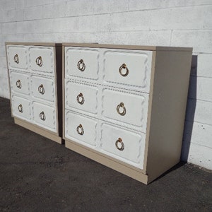 May include: Two white dressers with gold hardware and a light brown wood finish. The dressers have six drawers each with a raised panel design.