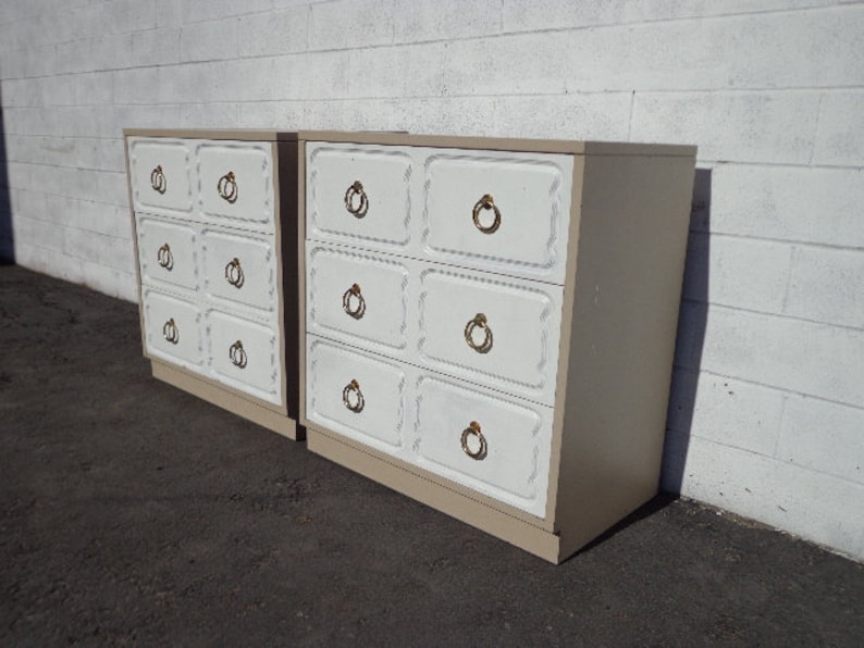 May include: Two white dressers with gold hardware and a light brown wood finish. The dressers have six drawers each with a raised panel design.