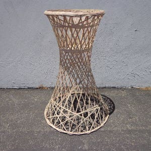 May include: White wicker end table with a round top and a woven design. The table has a unique, hourglass-shaped base.
