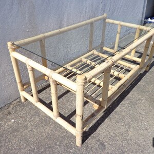 May include: A rectangular coffee table made of natural bamboo with a glass top. The table has a simple design with a woven bamboo base and a clear glass top.