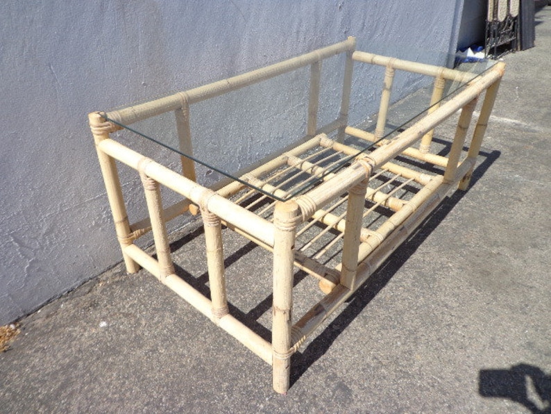 May include: A rectangular coffee table made of natural bamboo with a glass top. The table has a simple design with a woven bamboo base and a clear glass top.