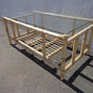 May include: A light brown bamboo coffee table with a glass top and a lower shelf. The table has a simple, rectangular design and is made of natural materials.
