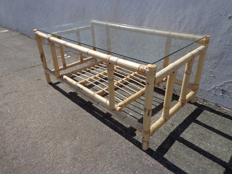 May include: A light brown bamboo coffee table with a glass top and a lower shelf. The table has a simple, rectangular design and is made of natural materials.