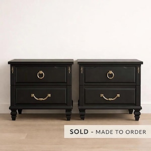 May include: Two black nightstands with two drawers each, featuring gold-colored hardware. The top drawer has a round pull, while the bottom drawer has a curved handle. The nightstands are on short, rounded legs. The text "SOLD - MADE TO ORDER" is at the bottom.