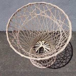 May include: A white wicker basket with a round, open top and a woven pattern. The basket is made of natural materials and has a rustic, vintage look.