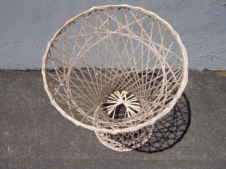 May include: A white wicker basket with a round, open top and a woven pattern. The basket is made of natural materials and has a rustic, vintage look.