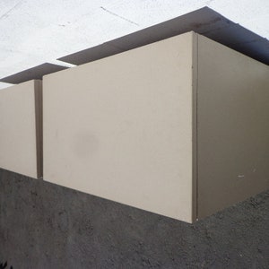 May include: Two beige wall-mounted cabinets with a simple design. The cabinets are closed and have a smooth surface.