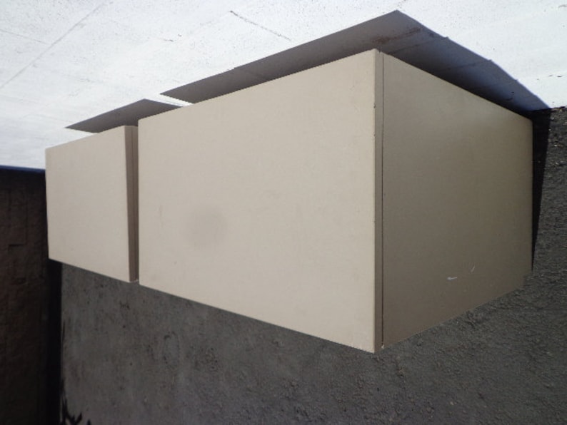 May include: Two beige wall-mounted cabinets with a simple design. The cabinets are closed and have a smooth surface.