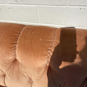 May include: A close-up of a brown tufted sofa with a shadow cast on the fabric.
